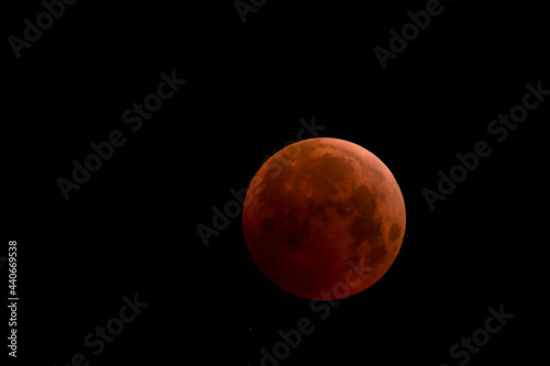 Fototapeta Naklejka Na Ścianę i Meble -  Full moon moving on the night sky dome with red shadow of earth sphere going across its silhouette during lunar eclipse in the perigeum
