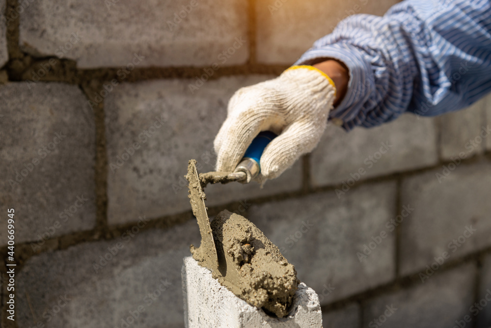 Masonry worker make concrete wall by cement block and plaster at construction site.