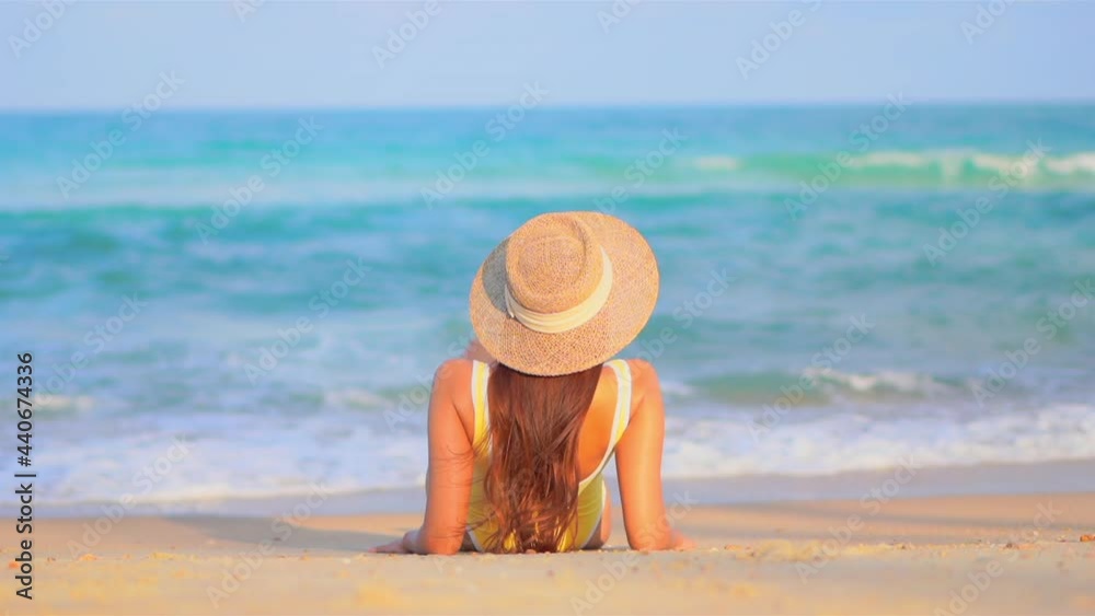 Back of Asian woman lying on the beautiful clean sand beach watching foamy sea tides rolling towards her, slow motion