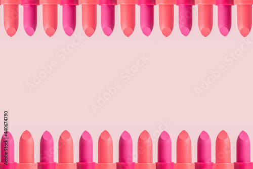 Lipstick frame on a pink background. Summer decorative cosmetics for lips. Set of coral and wine color lipsticks arranged in two lines.