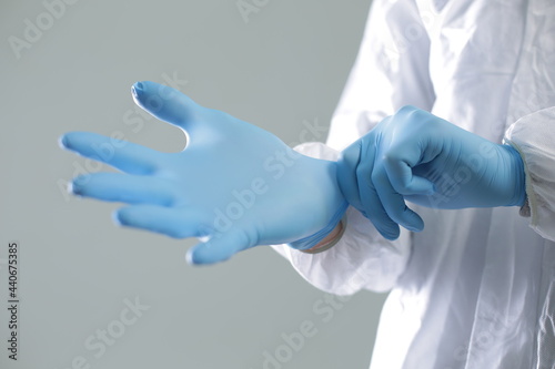 Doctor in a protective medical suit puts on blue rubber gloves