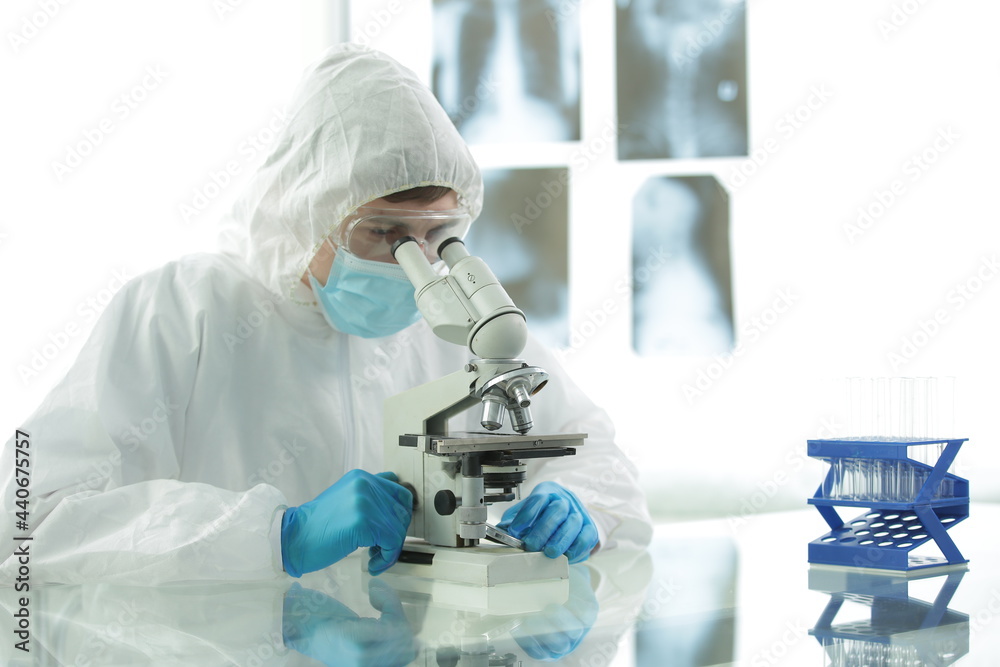 Doctor in a protective medical suit with gloves adjusts protective glasses near a microscope in a medical laboratory Doctor in a protective medical suit with gloves adjusts protective glasses near a microscope in a medical laboratory