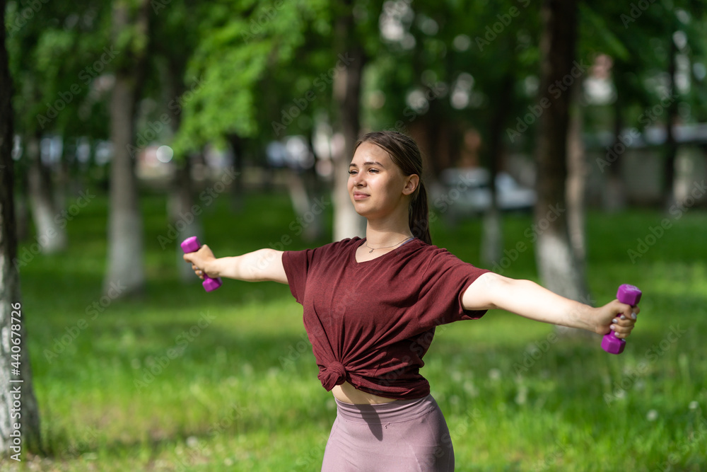 beautiful, smiling blonde girl holding dumbbells in her hands, doing sports in the fresh air beautiful, smiling blonde girl holding dumbbells in her hands, doing sports in the fresh air