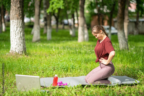 Young girl having online workout outdoors using laptop. Pilates or yoga video lesson on internet. Happy smiling girl practicing pilates lesson online in garden outdoors during quarantine © dinastiya