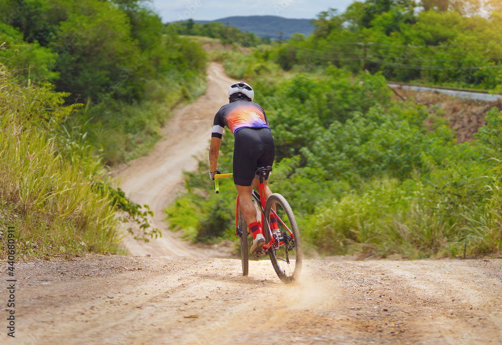 Obraz premium Asian man riding a bicycle on gravel road, he brakes down a hill.