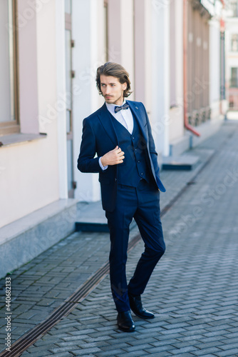 Handsome fashion businessman model dressed in elegant suit and posing on street. Metrosexual