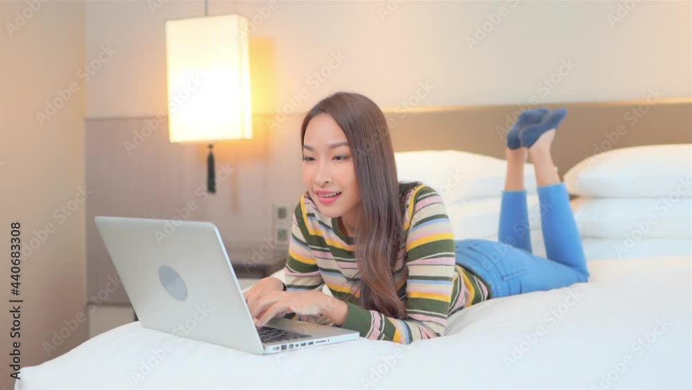 Slow-motion of relaxed Asian woman using her laptop computer lying on the bed with her legs raised at hotel room wearing casual clothes, working from home
Slow-motion of relaxed Asian woman using her laptop computer lying on the bed with her legs raised at hotel room wearing casual clothes, working from home