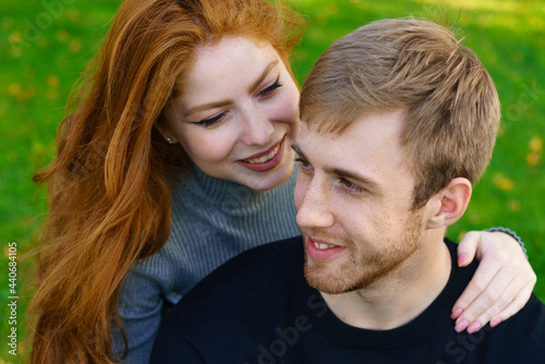 Happy young couple of Caucasian ethnicity man and woman in casual clothes sitting embracing in the park on green grass on a sunny day. Happy relationship between prana and a girl in nature © Екатерина Переславце