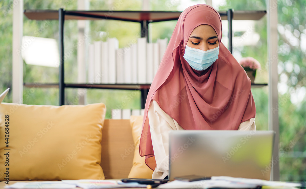 Young asian muslim woman relaxing using laptop computer working and video conference meeting online chat in quarantine for coronavirus wearing protective mask with social distancing at home Young asian muslim woman relaxing using laptop computer working and video conference meeting online chat in quarantine for coronavirus wearing protective mask with social distancing at home