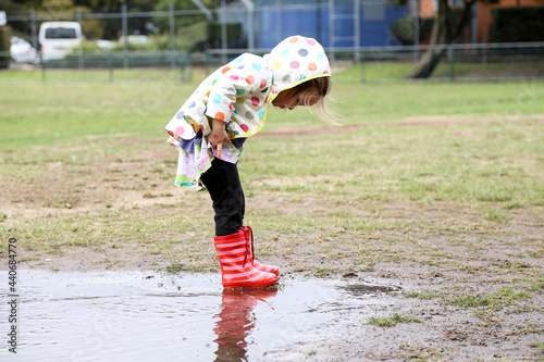 Young girl wearing spotted rain jacket playing in puddles