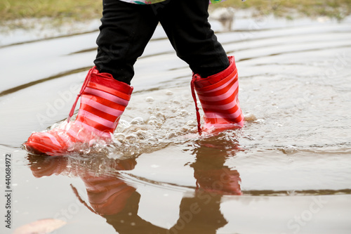 Close-up shot of girl's feet in red gumboots standing in puddle