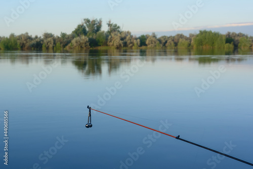Fishing rod with silver bell against background of river. Selective focus