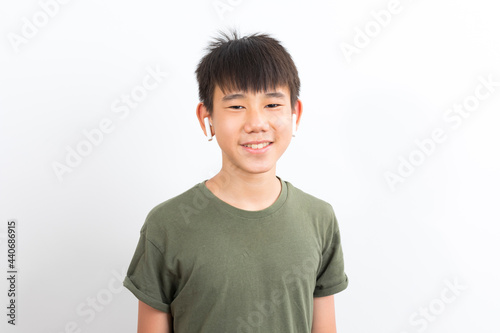joyful Asian boy 10-12y wearing earpods smiling on white background.