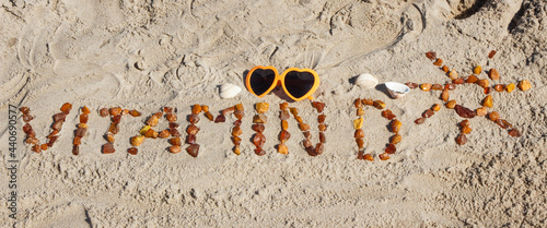 Inscription vitamin D with shape of sun and sunglasses on sand at beach. Prevention of vitamin D deficiency