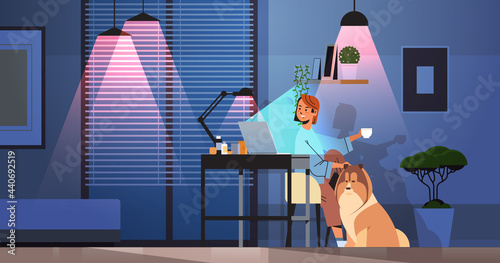 businesswoman freelancer looking at laptop screen woman sitting at workplace near dog in dark night room