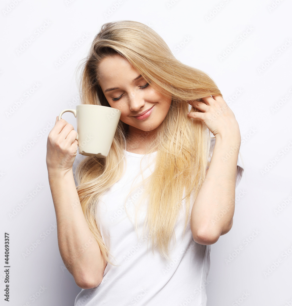 Young blonde woman holds white cup. Beautiful girl with long white hair is holding cup with tea. Young blonde woman holds white cup. Beautiful girl with long white hair is holding cup with tea.