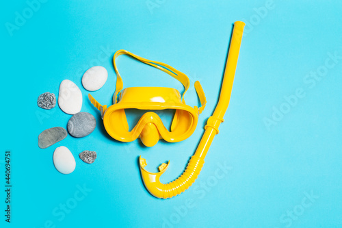 Top view of yellow diving mask with snorkel near stones on blue background.