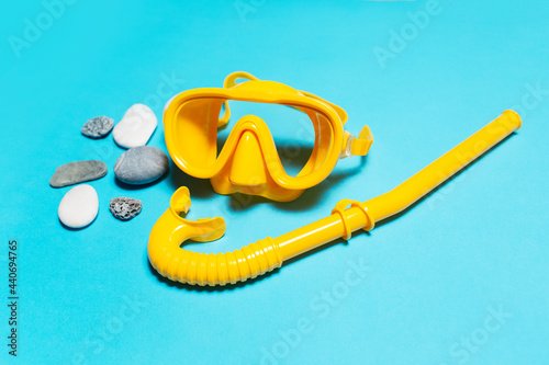 Close-up of yellow diving mask with snorkel near stones on blue background.