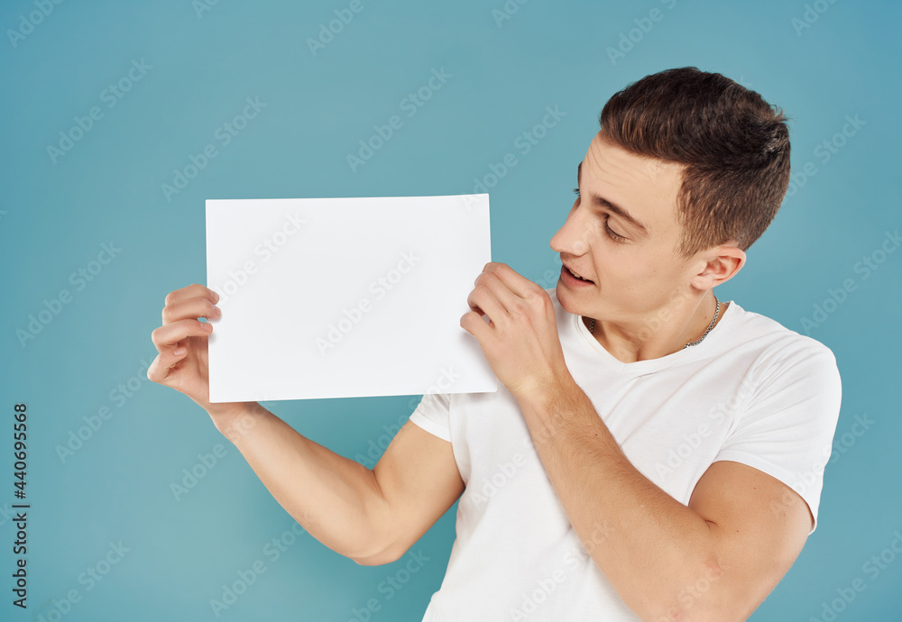 handsome man in white t-shirt with white sheet of paper in his hands paperspace blue background handsome man in white t-shirt with white sheet of paper in his hands paperspace blue background