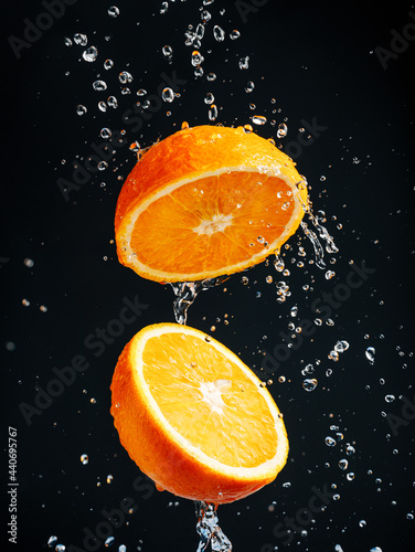 Wet and juicy orange cut in two halves flying in the air with water drops splashing isolated on contrast black background. Summer citrus fruit refreshment. Creative food or drink concept.