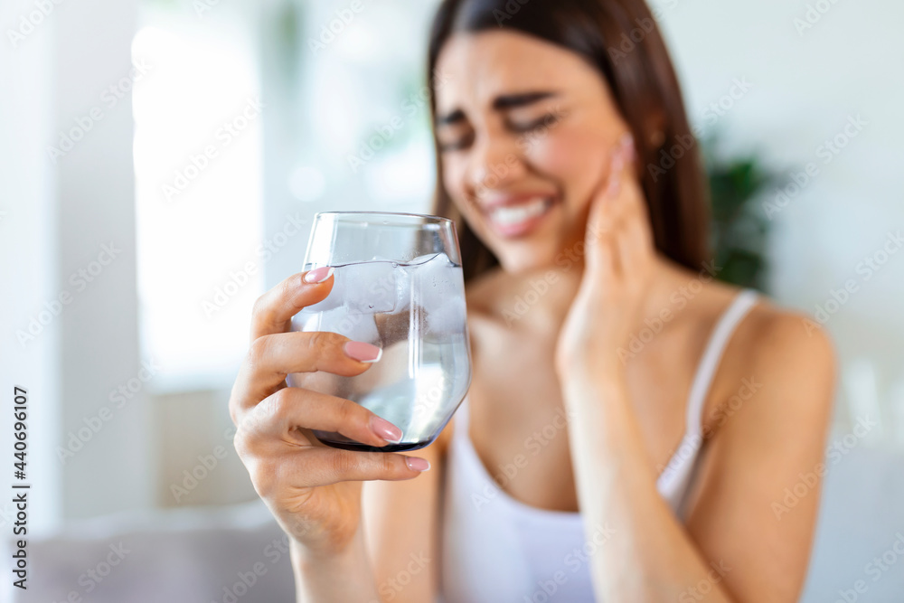 Young woman with sensitive teeth and hand holding glass of cold water with ice. Healthcare concept. woman drinking cold drink, glass full of ice cubes and feels toothache, pain