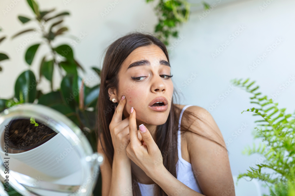 Shot of a young woman squeezing a pimple in front of the mirror, A young woman looking shocked as she examines her skin Shot of a young woman squeezing a pimple in front of the mirror, A young woman looking shocked as she examines her skin