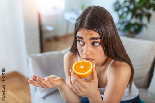 Sick woman trying to sense smell of half fresh orange, has symptoms of Covid-19, corona virus infection - loss of smell and taste. One of the main signs of the disease. photo