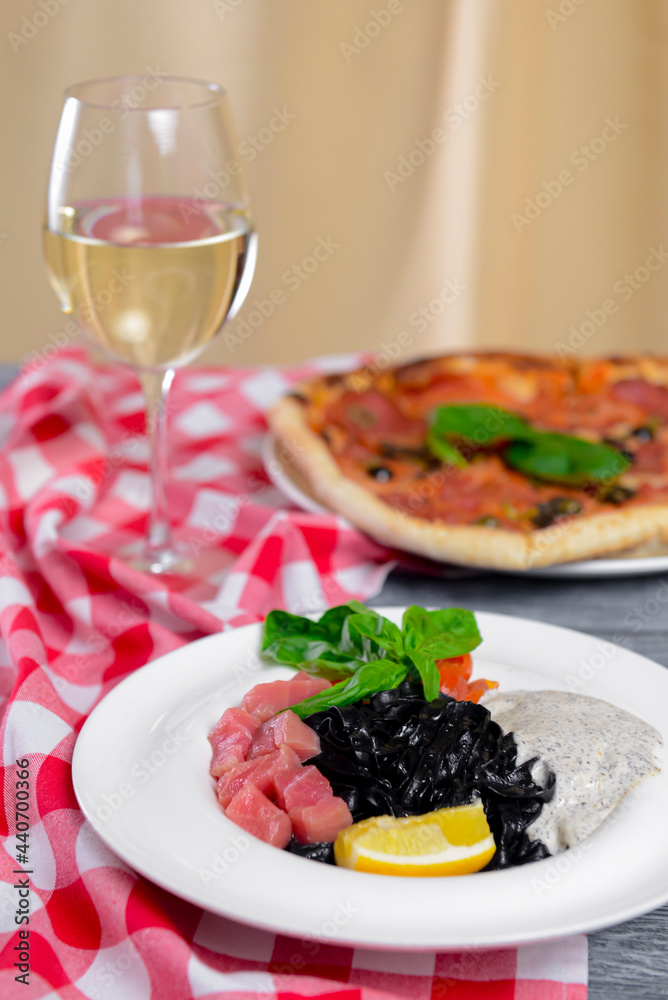 Squid Ink Black Pasta with seafood served on a white plate with a glass of white wine. Squid Ink Black Pasta with seafood served on a white plate with a glass of white wine.