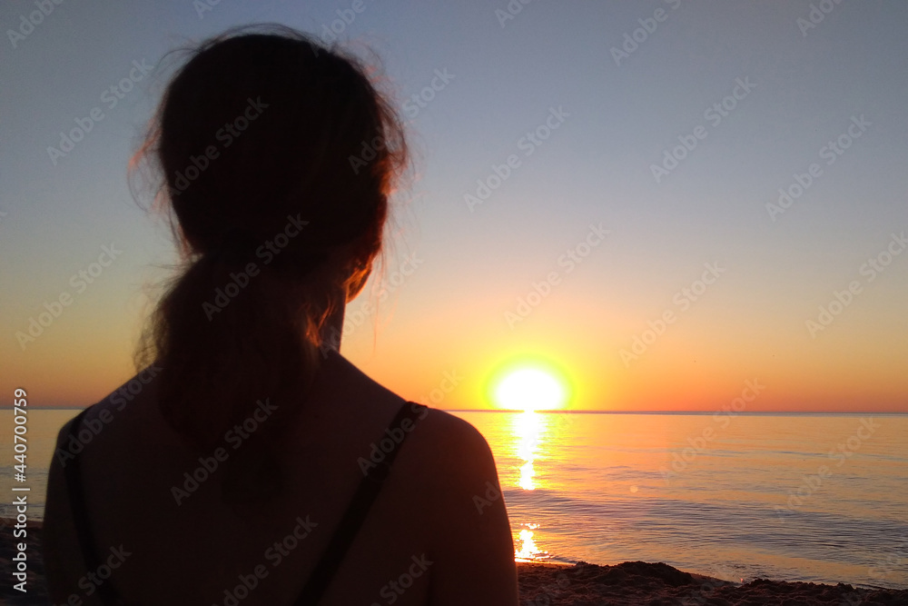 The silhouette of a young woman against the backdrop of a beautiful sunset on the Baltic Sea