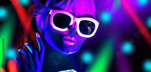 Disco dancer in neon light in night club Fashion model woman in neon light, portrait of beautiful girl with fluorescent make-up, Body Art design in UV, sunglasses, colorful make up.  photo