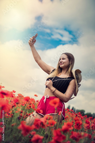 Ukrainian woman in sportswear and straw hat taking a photo selfie with smartphone in poppies field