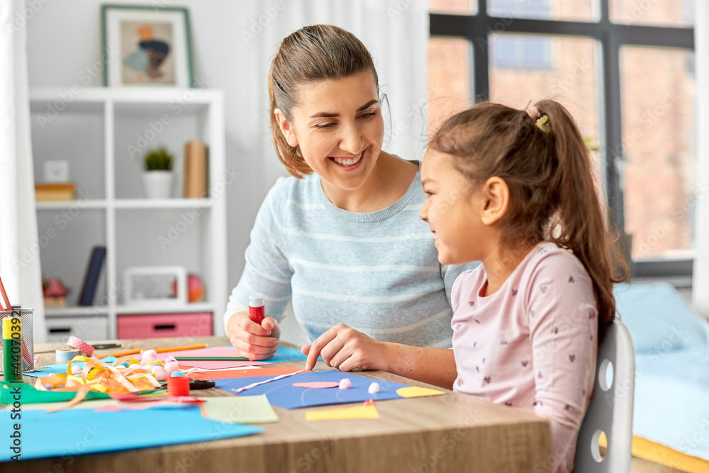 family, art and craft concept - mother spending time with her little daughter with glue making applique of color paper at home