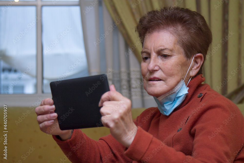 senior woman with medical mask making a video call from home to her relatives in times of pandemic and confinement senior woman with medical mask making a video call from home to her relatives in times of pandemic and confinement