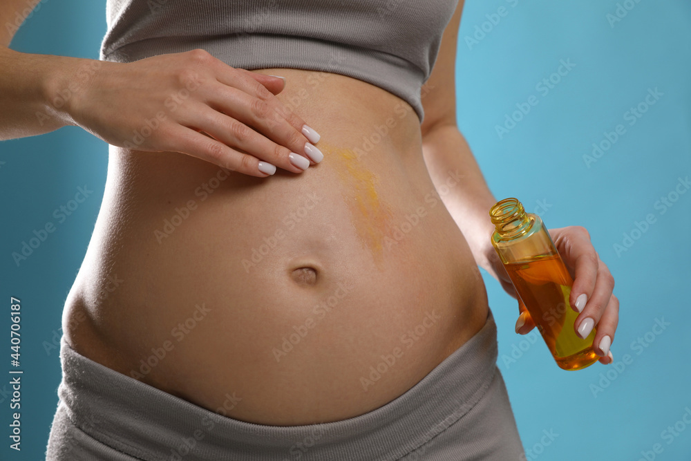 Pregnant woman applying cosmetic product on belly against light blue background, closeup - obrazy, fototapety, plakaty 
