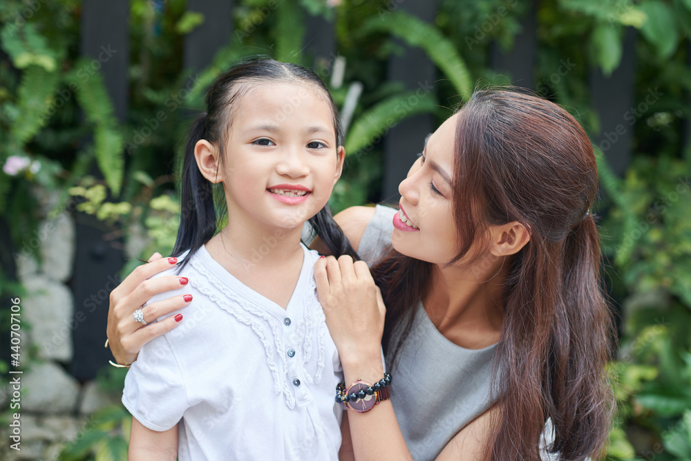 Happy young woman looking at her preteen daughter standing outdoors and smiling at camera Happy young woman looking at her preteen daughter standing outdoors and smiling at camera