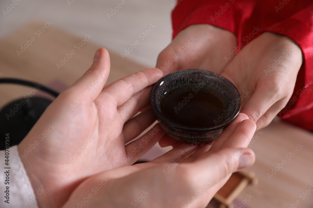 Master giving freshly brewed tea to guest during ceremony at table, closeup Master giving freshly brewed tea to guest during ceremony at table, closeup