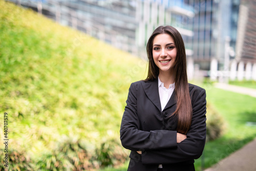 Smiling young woman near a grass field and a glass office building © Minerva Studio