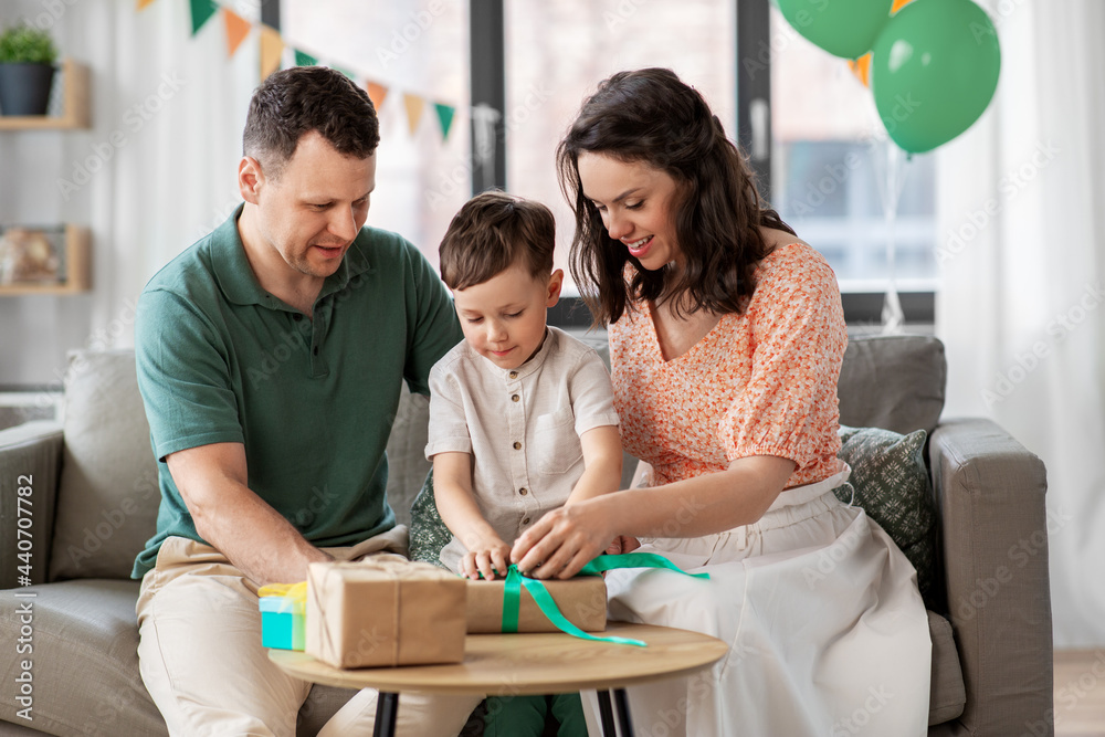 Obraz premium family, holidays and people concept - happy mother, father and little son opening birthday presents at home party