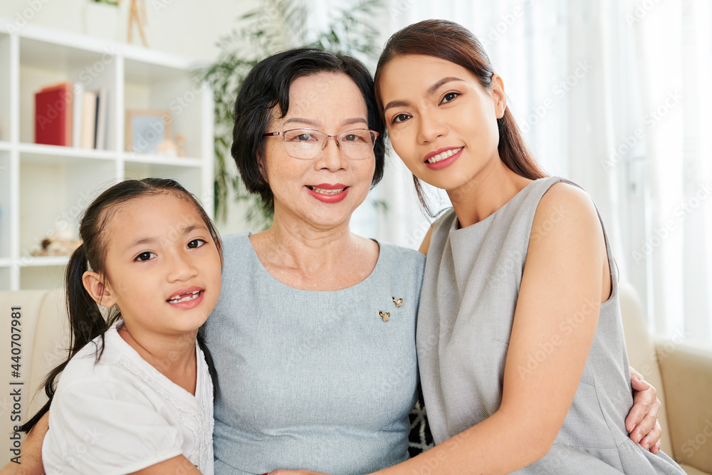 Portrait of three generations of one family, grandmother, mother and granddaughter hugging and smiling at camera Portrait of three generations of one family, grandmother, mother and granddaughter hugging and smiling at camera