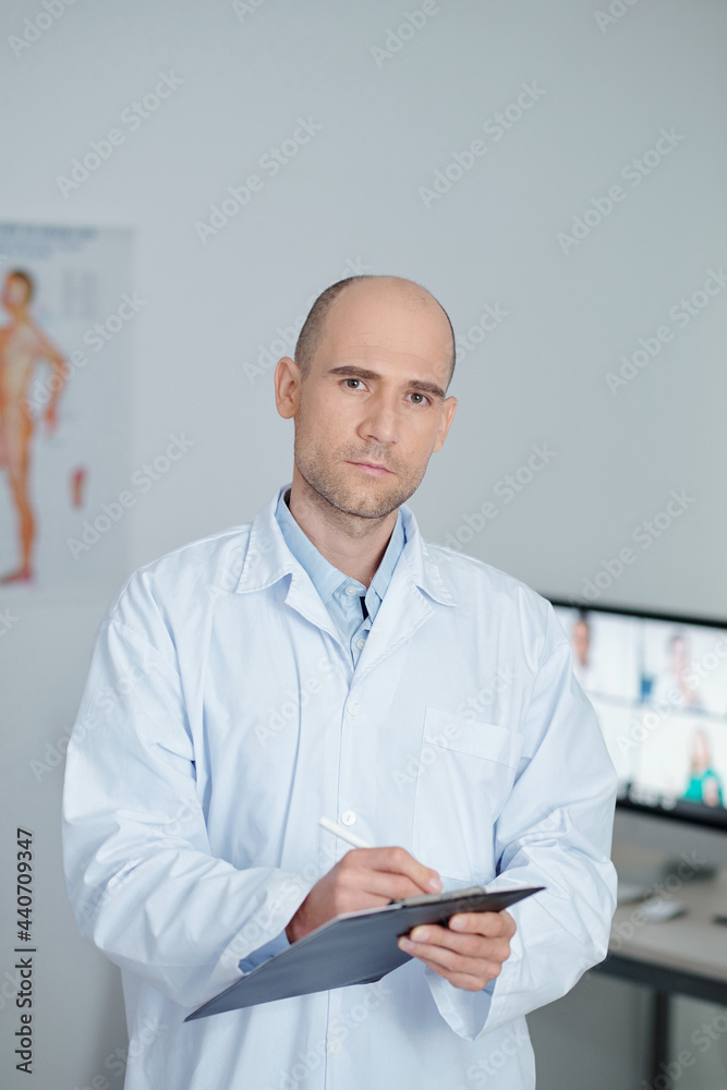 Portrait of serious general practitioner in white labcoat writing patients data in document Portrait of serious general practitioner in white labcoat writing patients data in document