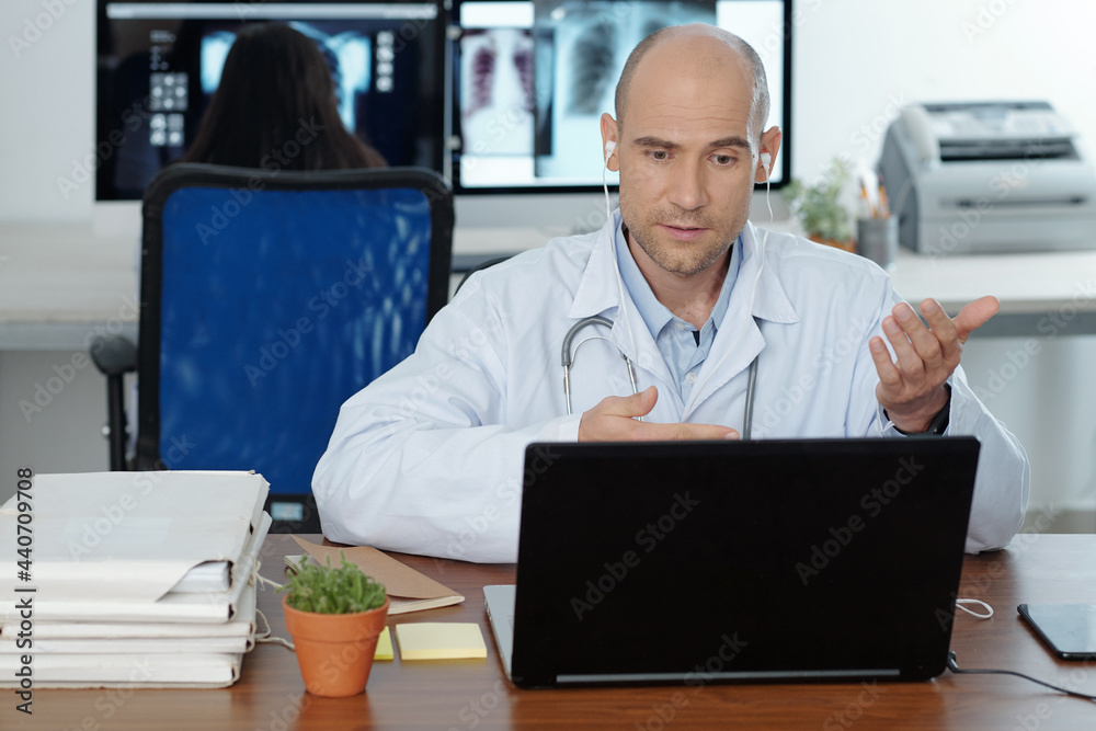 Fototapeta premium Doctor sitting at desk, having video call with colleague or patient and discussing disease treatment