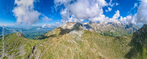 Fototapeta Naklejka Na Ścianę i Meble -  Vibrant aerial panoramic of the Alps during springtime. Snow capped peaks, forest covered valley and glacier fed streams and waterfalls