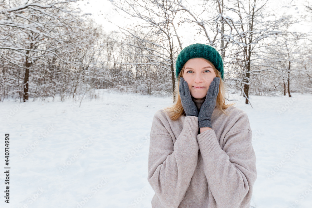 Obraz premium Happy young woman wearing in winter knitted hat and sweater posing over nature background, Looking at camera and smile. Travel and active life concept. Outdoors