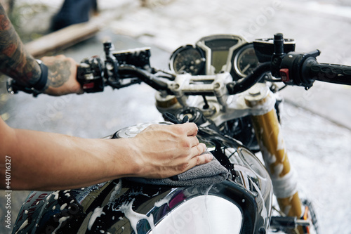 Hands of man wiping off cleaning foam from his motorcycle with soft cloth