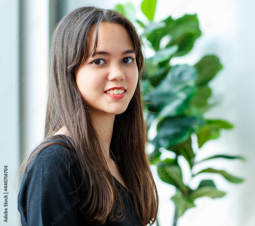 Front view portrait shot of an attractive smiling junior young Thai-Turkish teenager wearing trendy casual clothes sitting on the red couch and looking at camera in studio with windows background. Front view portrait shot of an attractive smiling junior young Thai-Turkish teenager wearing trendy casual clothes sitting on the red couch and looking at camera in studio with windows background.