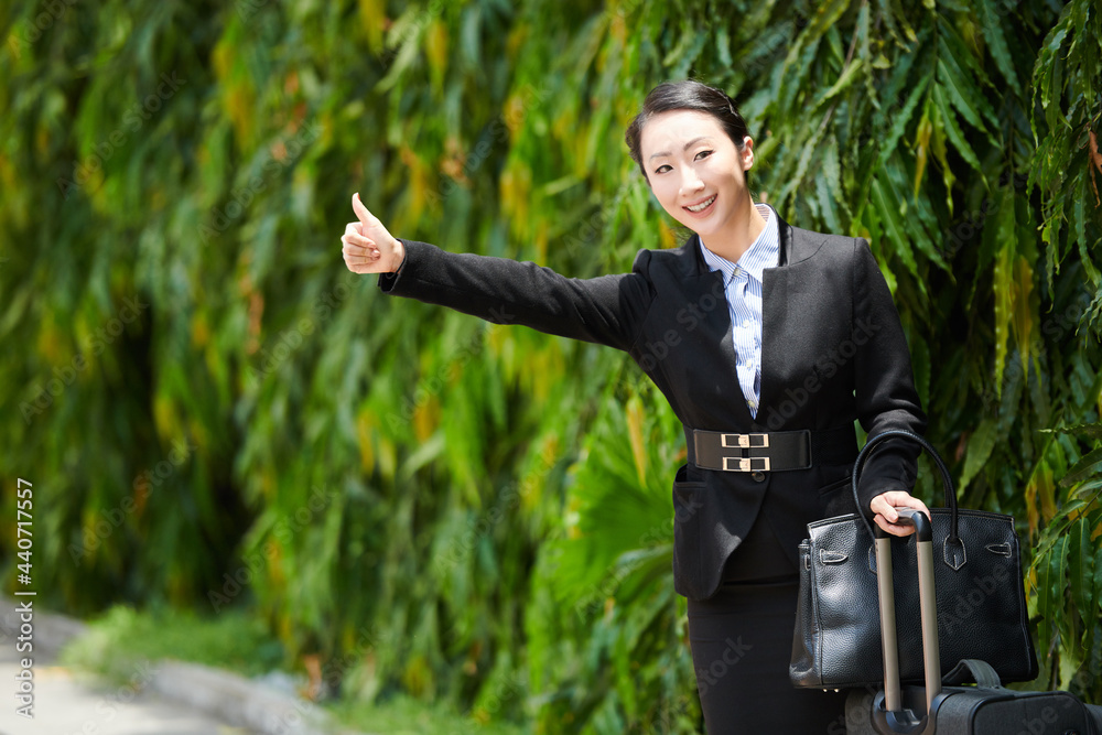 Smiling young businesswoman making thumbs-up gesture when trying to catch a taxi car to airport or hotel Smiling young businesswoman making thumbs-up gesture when trying to catch a taxi car to airport or hotel