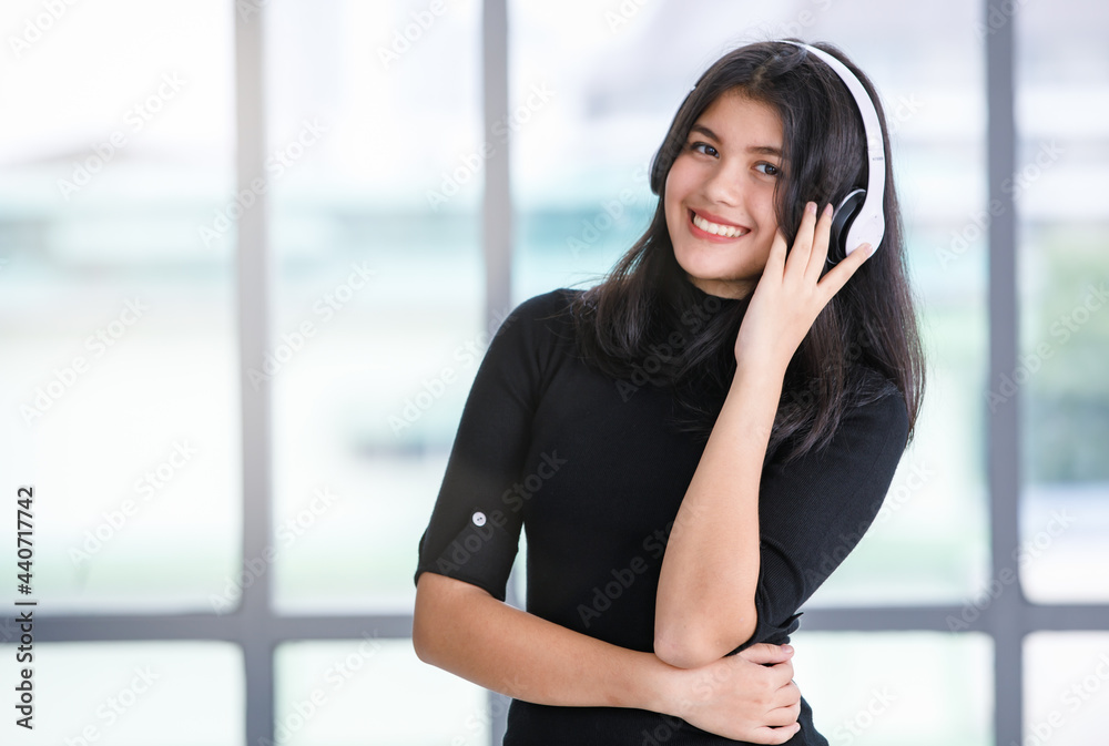 Portrait shot of cute smiling young Thai-Turkish teenager enjoying listening to music with a headset while looking at camera. Junior girl model with casual black clothes posing in the studio Portrait shot of cute smiling young Thai-Turkish teenager enjoying listening to music with a headset while looking at camera. Junior girl model with casual black clothes posing in the studio