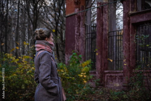 A young woman looks at the ruins of an old building - an abandoned family home. The concept of a belated return to basics