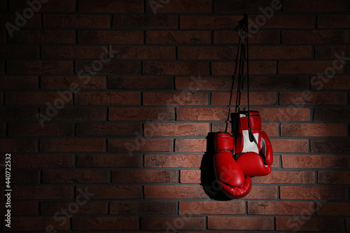 Pair of red boxing gloves hanging in spotlight on brick wall, space for text © New Africa