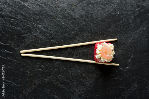 roll with shrimp and chopsticks on a black slate background with copy space.